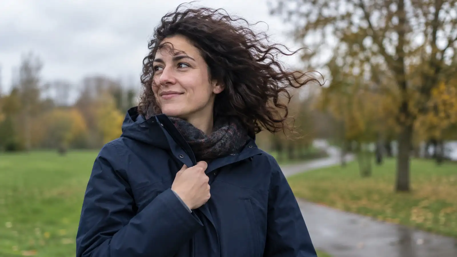 Frau mit Locken bei Wind. Neutrale Alltagskulisse ohne behaupteten Aufnahmeort.