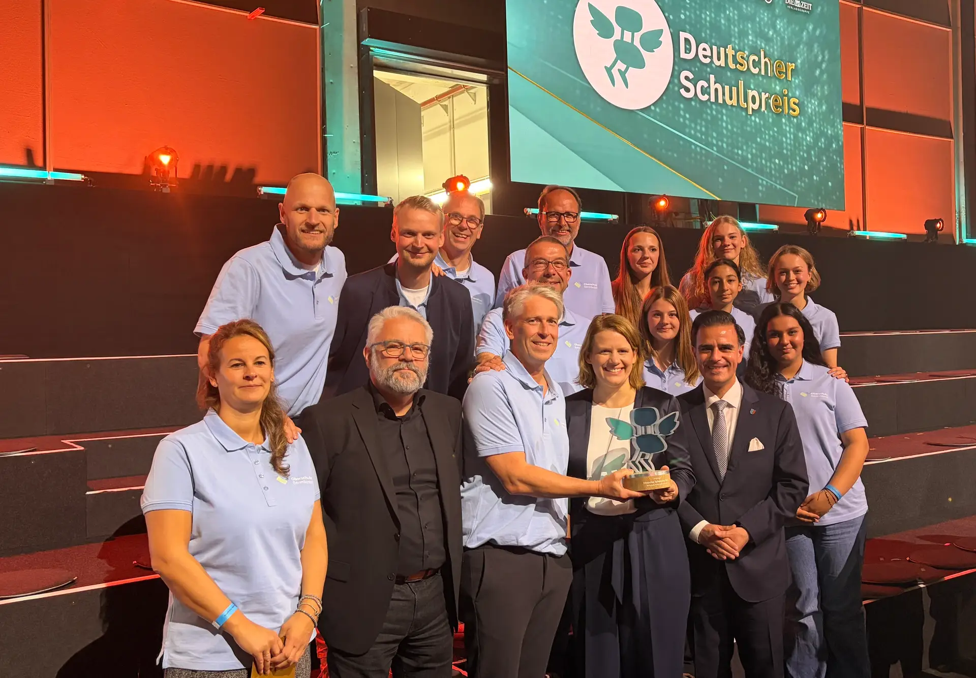 Eine Gruppe aus Schülerinnen, Schülern und Erwachsenen steht bei der Verleihung des Deutschen Schulpreises vor einer Bühne; vorn wird eine Trophäe gehalten.